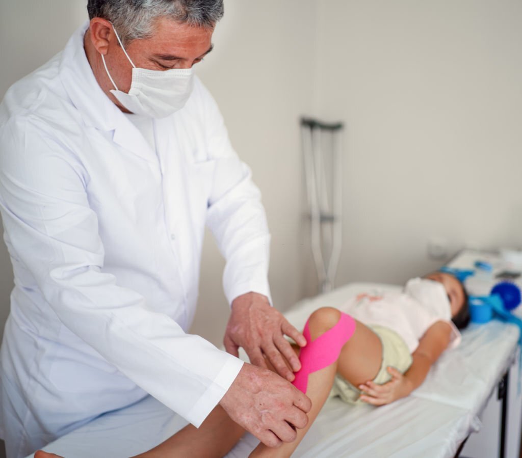 Male Physiotherapist Taping Pink Medical Tape On A Patient's Knee